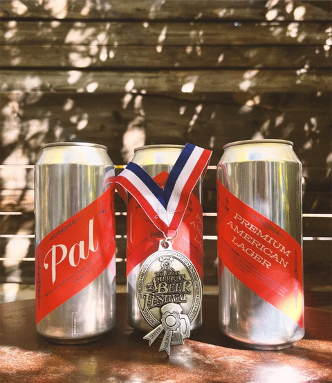 Three beer cans with red labels and a silver medal on a wooden surface.