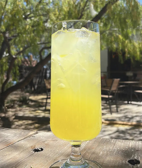 Glass of yellow lemonade with ice on a wooden table outdoors