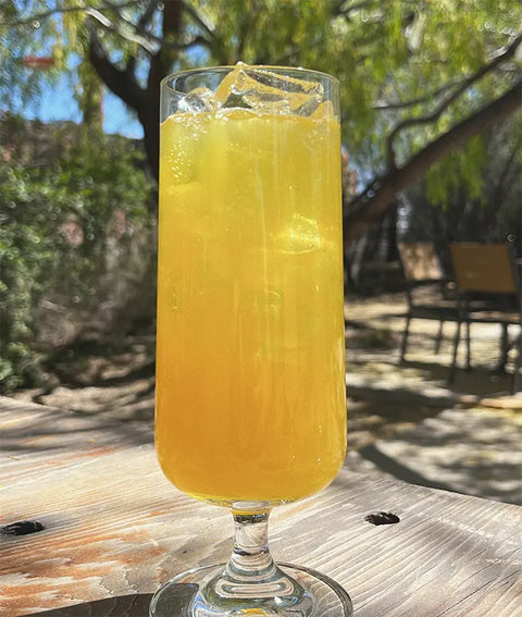 Glass of yellow drink with ice on a wooden table outdoors