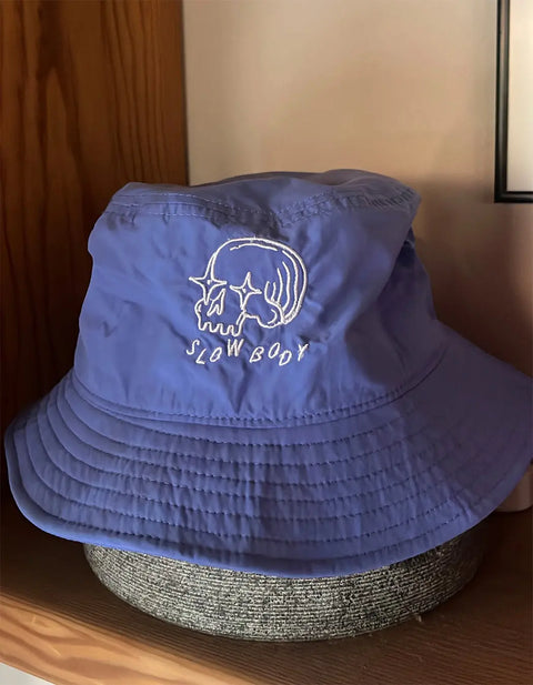 Blue bucket hat with 'SLOW BODY' logo on a wooden surface